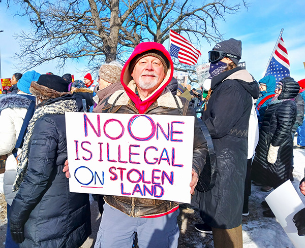 Kent carrying a sign reading "No one is illegal on stolen land"